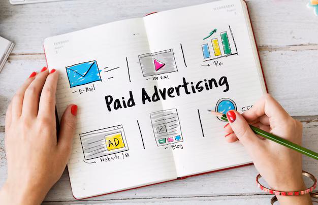 A lady painting in her note book on the topic of "Paid Advertising" by penciled wearing hand braclete and showing the value of Paid Advertising in Digital marketing for real estate companies